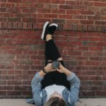 woman in black long sleeve shirt and blue denim jeans sitting on brown brick wall