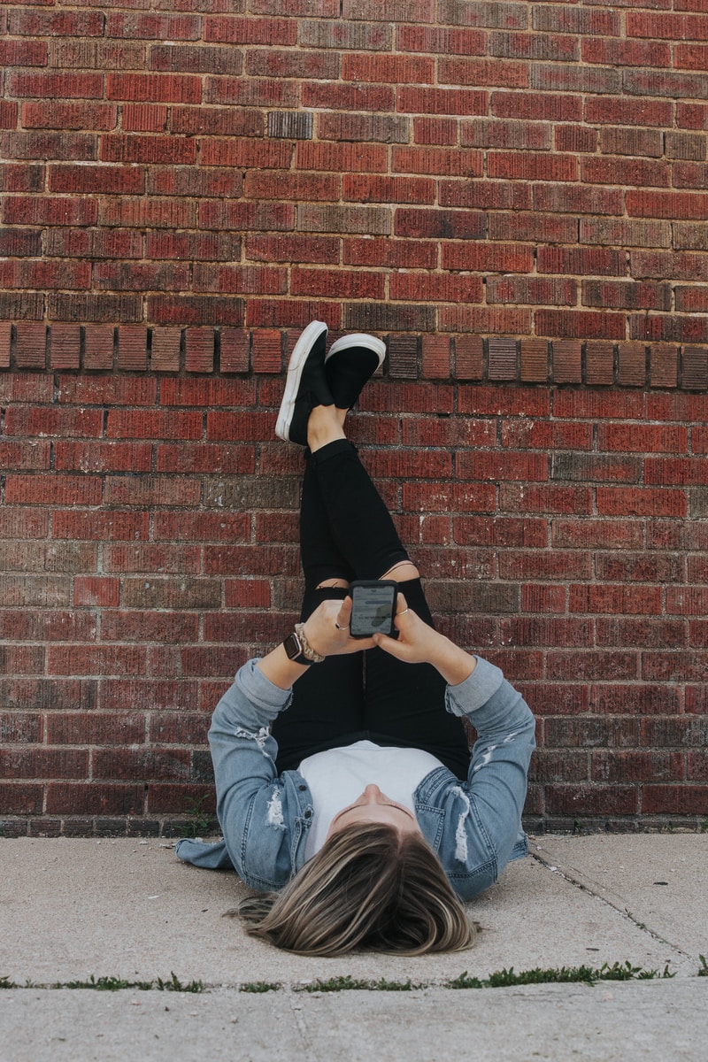 woman in black long sleeve shirt and blue denim jeans sitting on brown brick wall