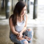 woman in white tank top and blue denim jeans sitting on concrete floor during daytime