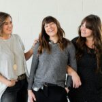 3 women smiling and standing beside white wall